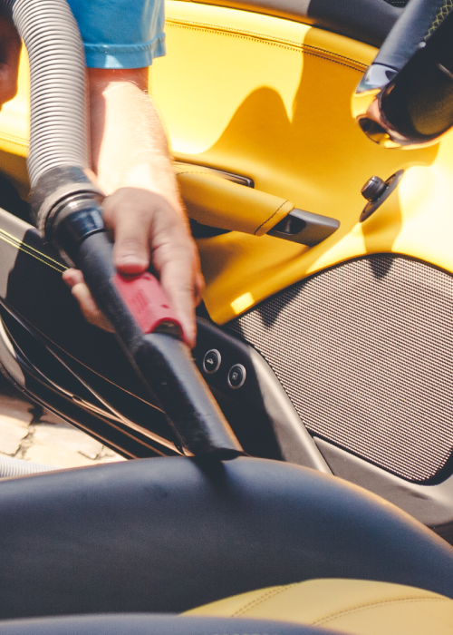 Hand vacuuming a yellow car seat with a red and black nozzle