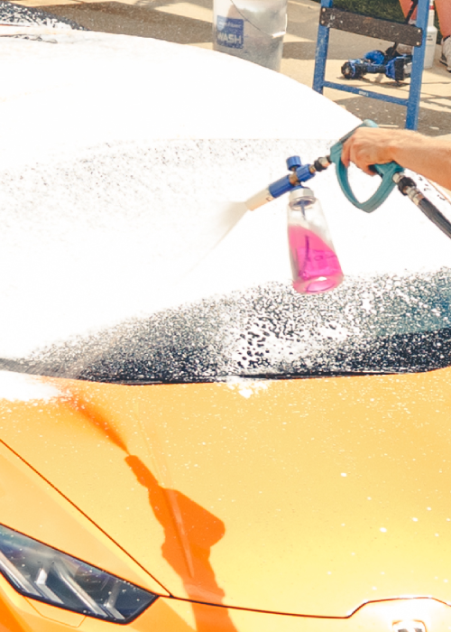 Person spraying foam on a yellow car at a car wash