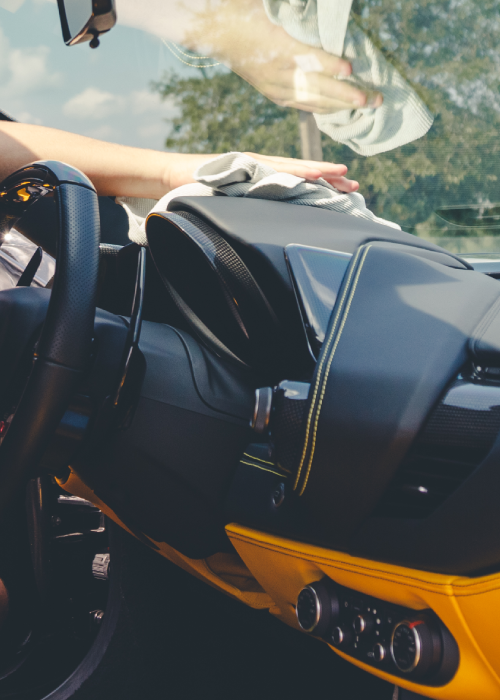 Black and orange sports car interior with windshield, parked outdoors under trees