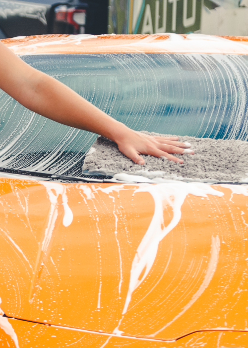 Person washing an orange car with soapy water and a sponge