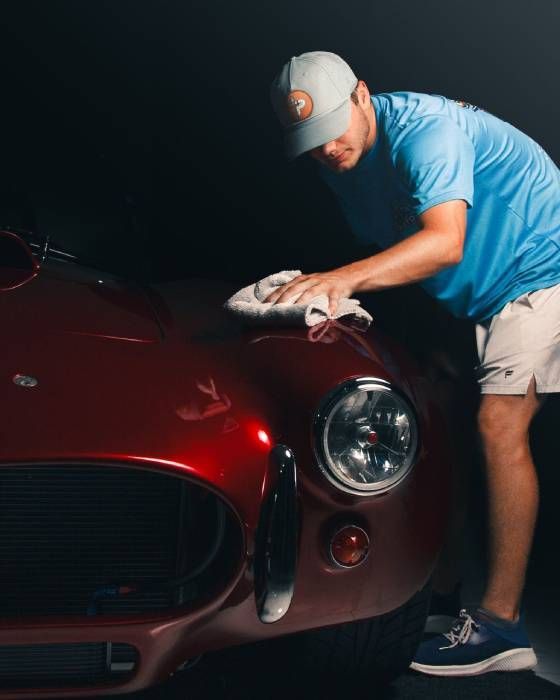 Man polishing a red vintage sports car with a cloth in a dark garage