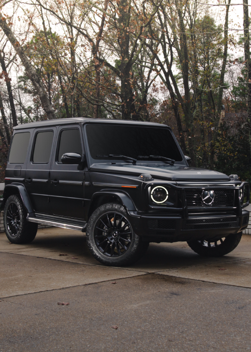 Black Mercedes G-Wagon parked on a driveway with trees in the background