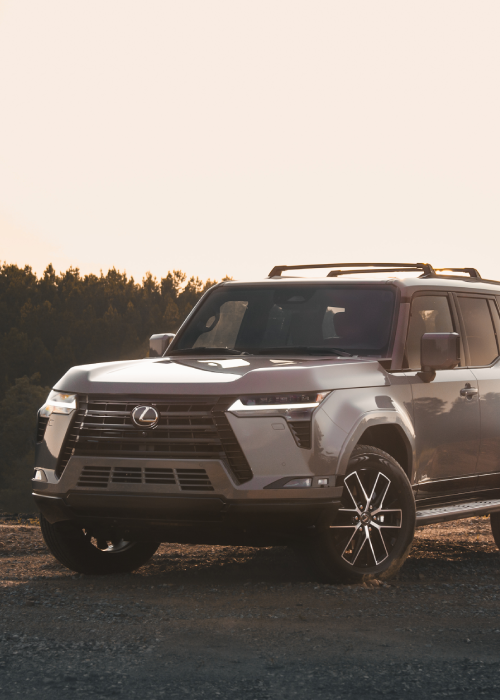 Silver Lexus SUV parked on a road at sunset with trees in the background