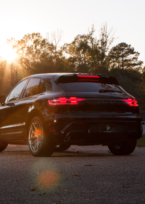 Black SUV driving at sunset on a road with trees in the background