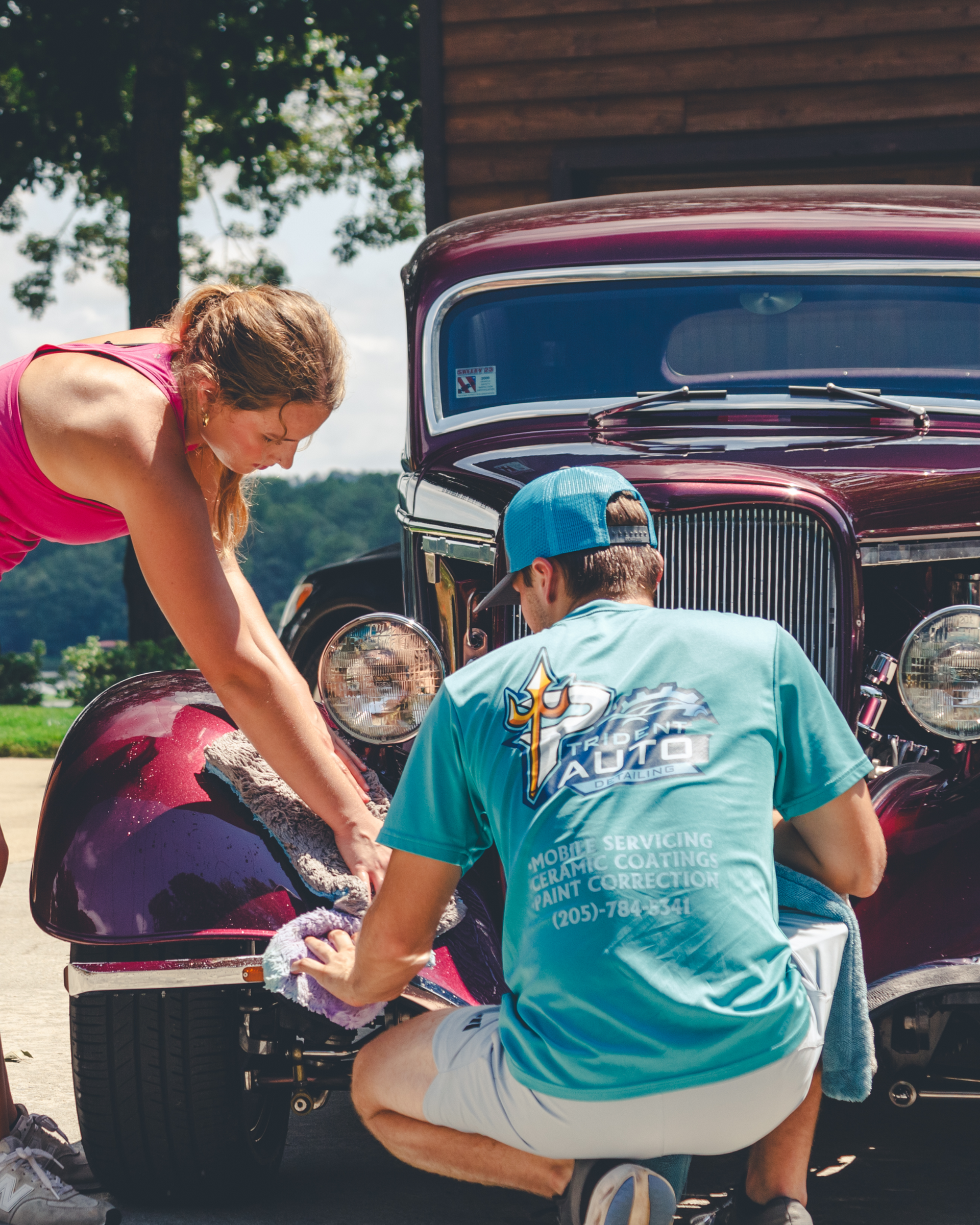 Two people working on the front of a maroon vintage car outdoors