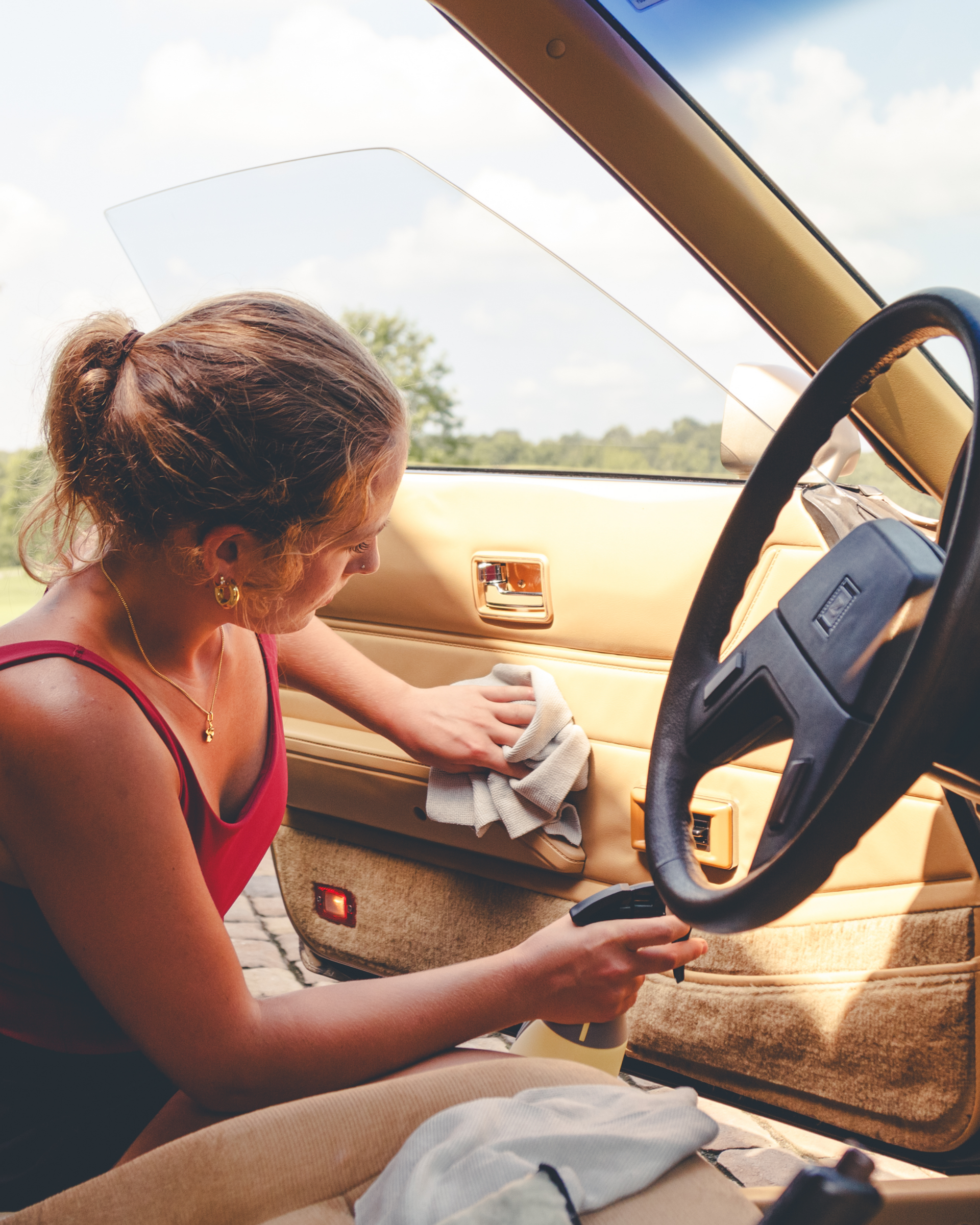 Person cleaning the interior of a tan car door while sitting in the driver's seat.