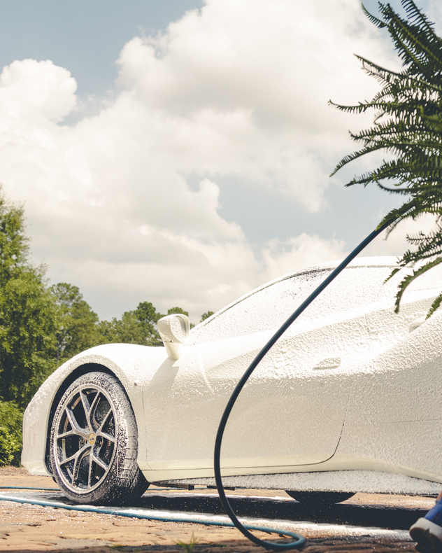 Car being spray-washed with thick white foam, covering the side and wheel