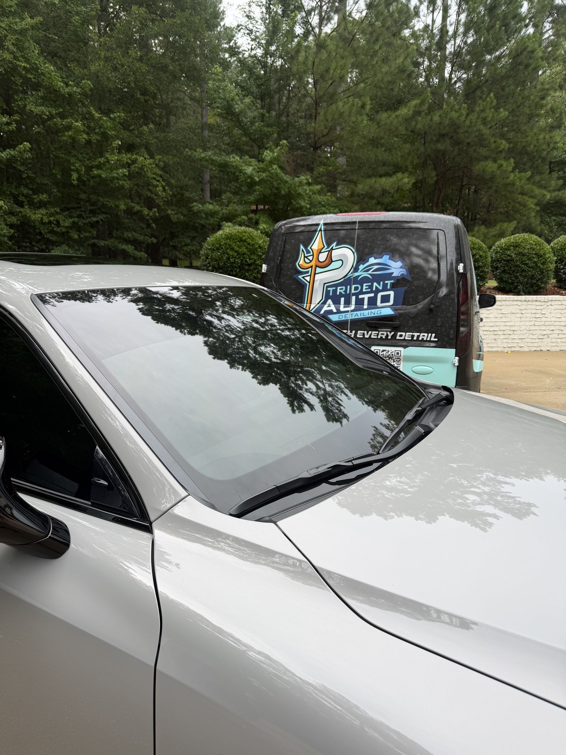 Silver car in front of a black auto service van in a wooded parking area