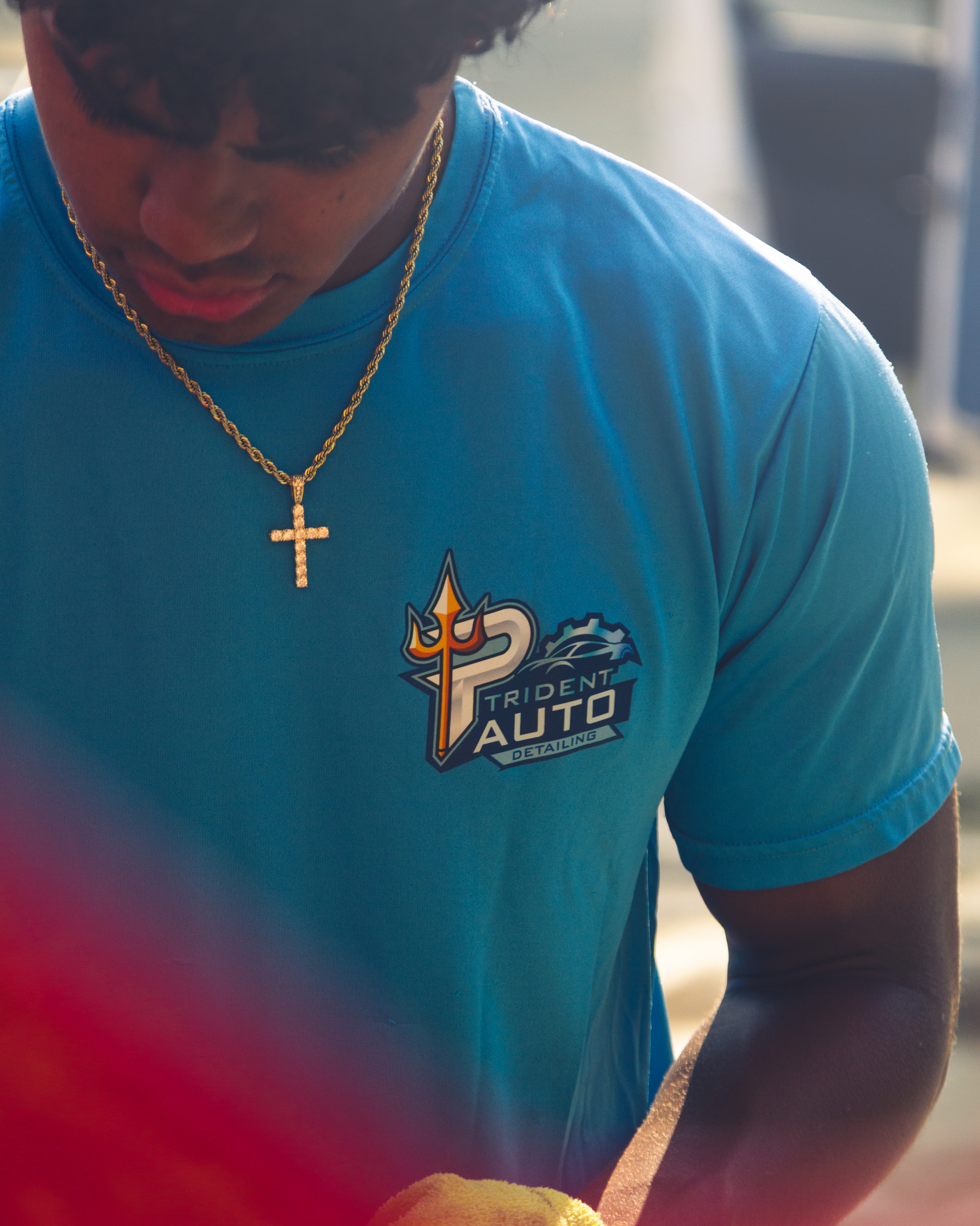 Person in a blue shirt with a gold cross necklace, looking down indoors.