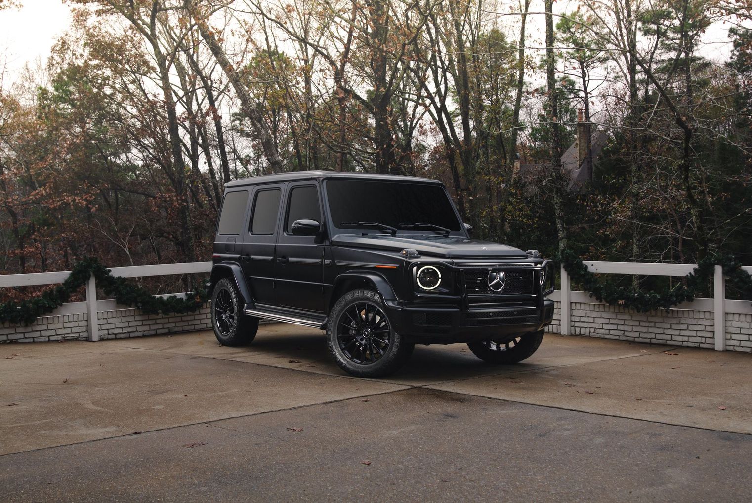 Black Mercedes G-Class SUV parked on a driveway with trees and stone fences in the background