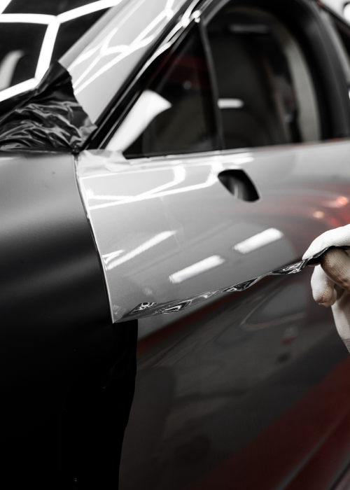 Hand applying black vinyl wrap to a white car door indoors