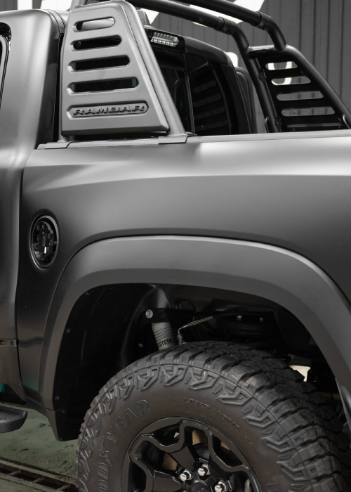 Close-up of a silver off-road truck with black wheels and fender flare inside a garage