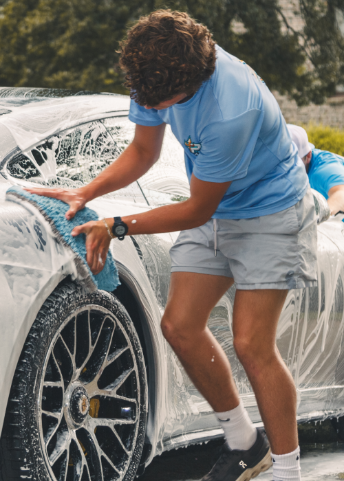 Person washing a black sports car with blue soap suds outdoors