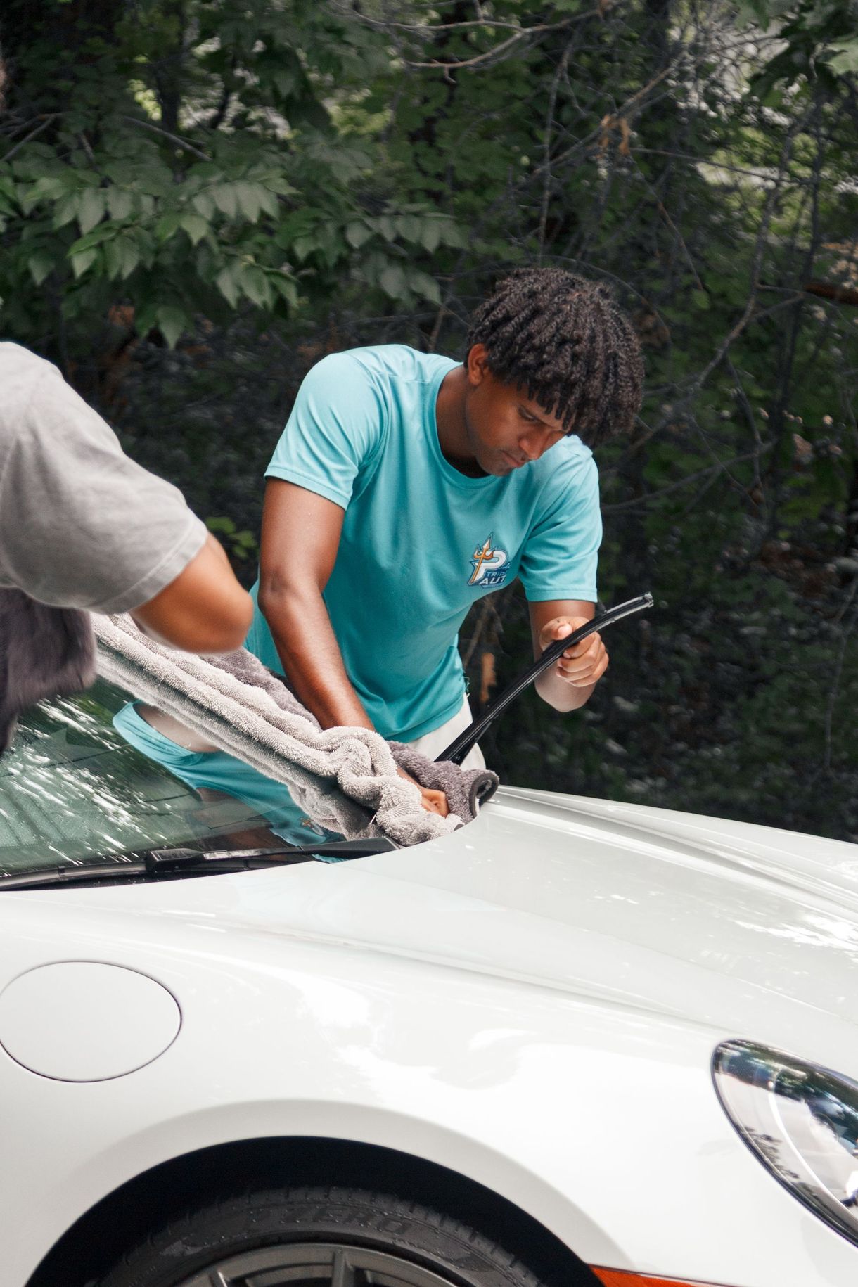 Person cleaning a white car windshield outdoors with a squeegee and cloth