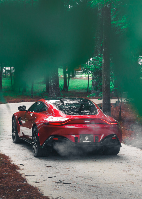 Red sports car drifting on a forest road, kicking up smoke beside tall trees