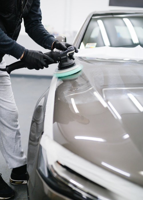 Detailing a gray car with a rotary polisher in a garage