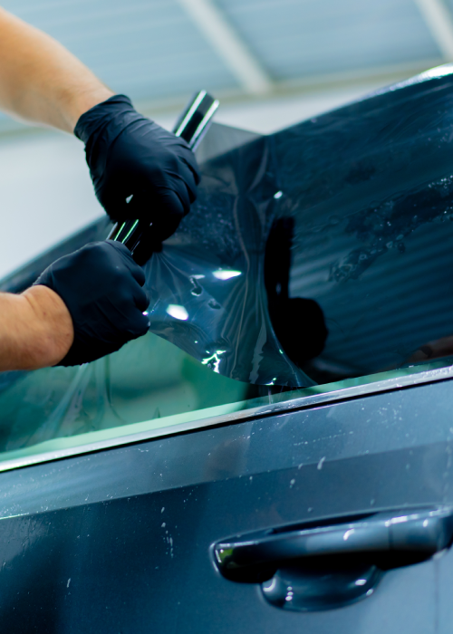 Gloved hands applying dark window tint film to a car side window