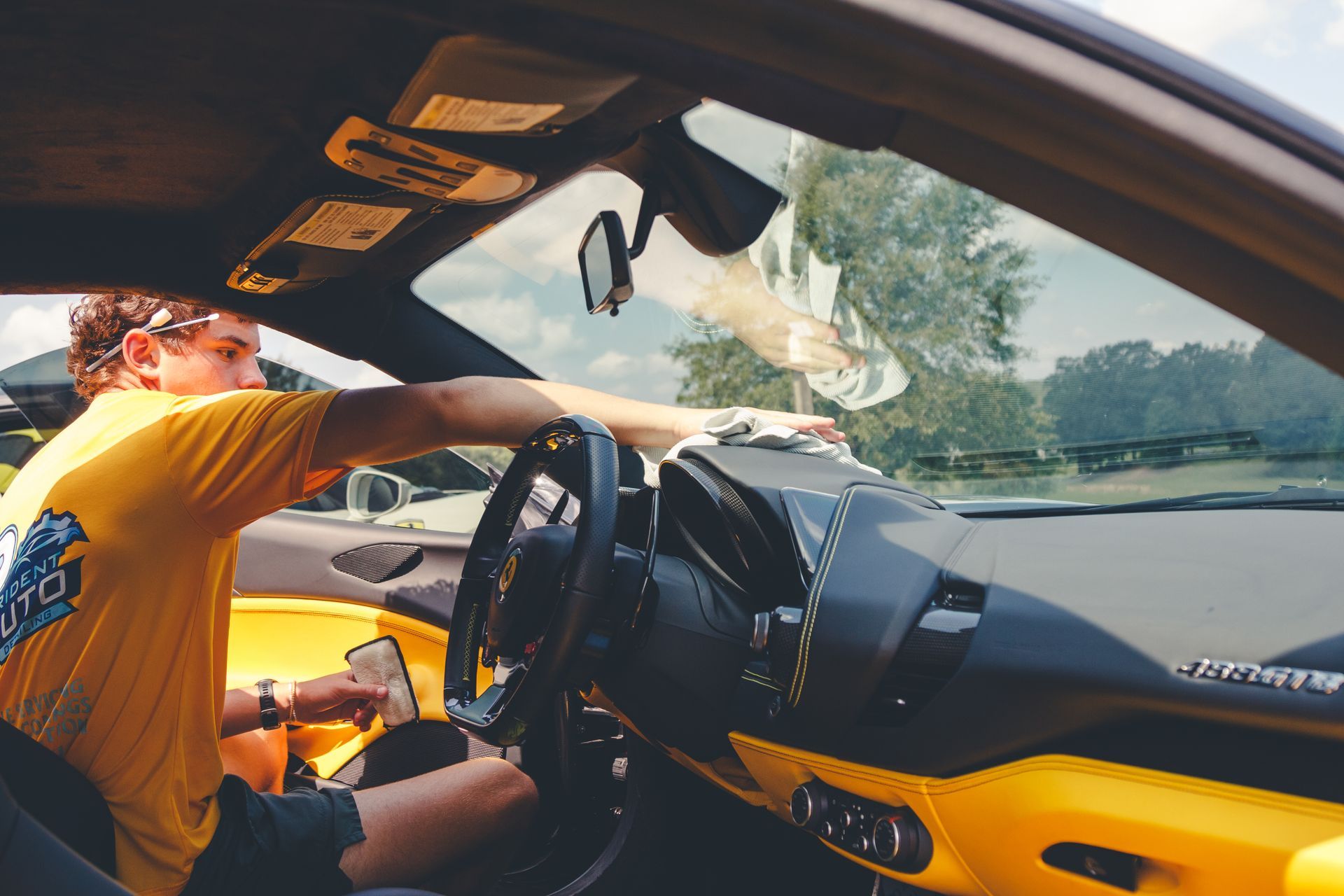 Driver leaning into a black and yellow sports car interior, viewed through the open window.