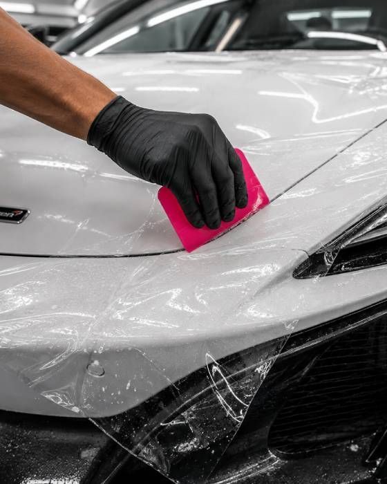 Hands using a utility knife to cut clear plastic film on a white surface