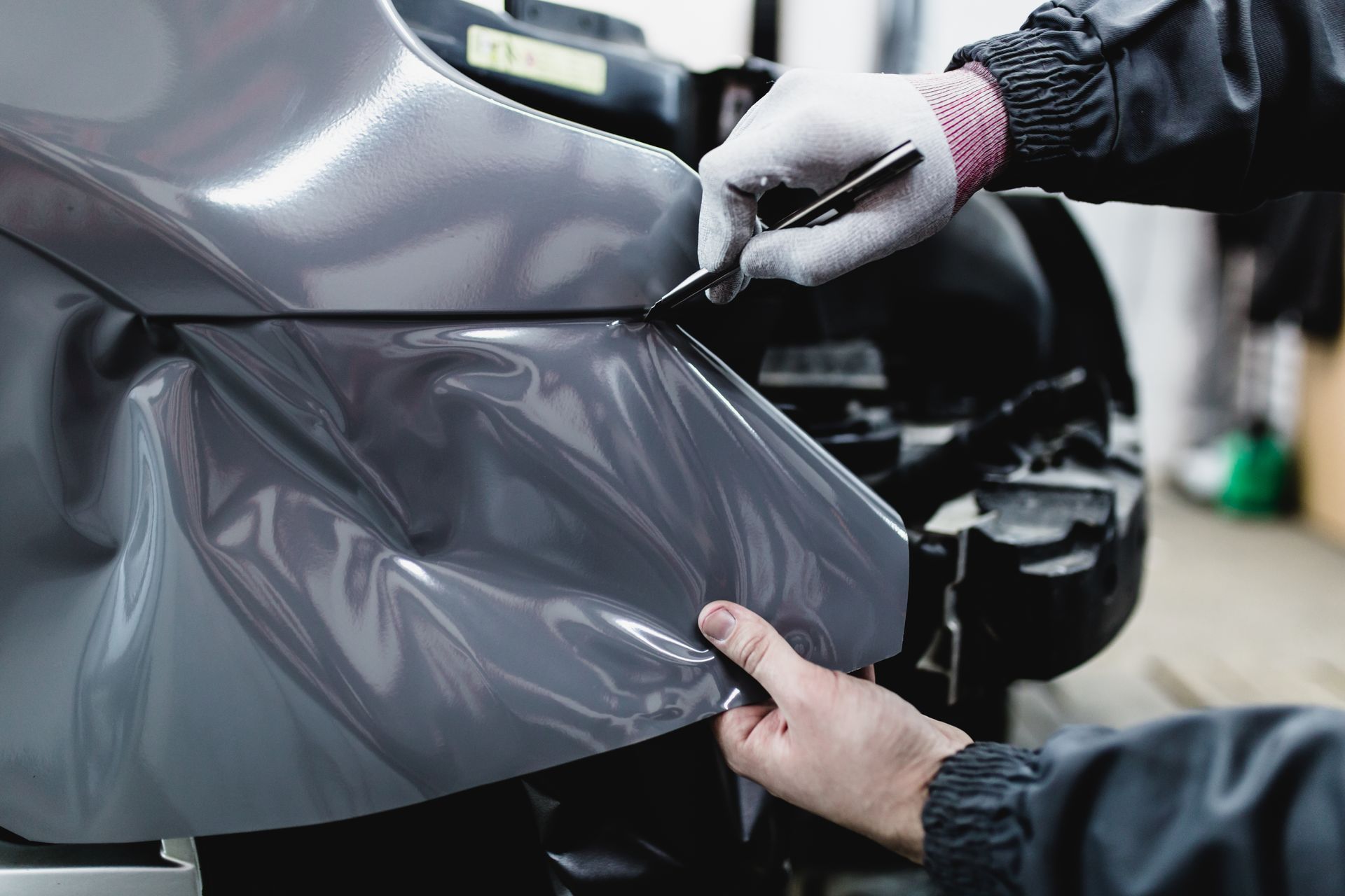 Hands apply black vinyl wrap to a car panel in a workshop
