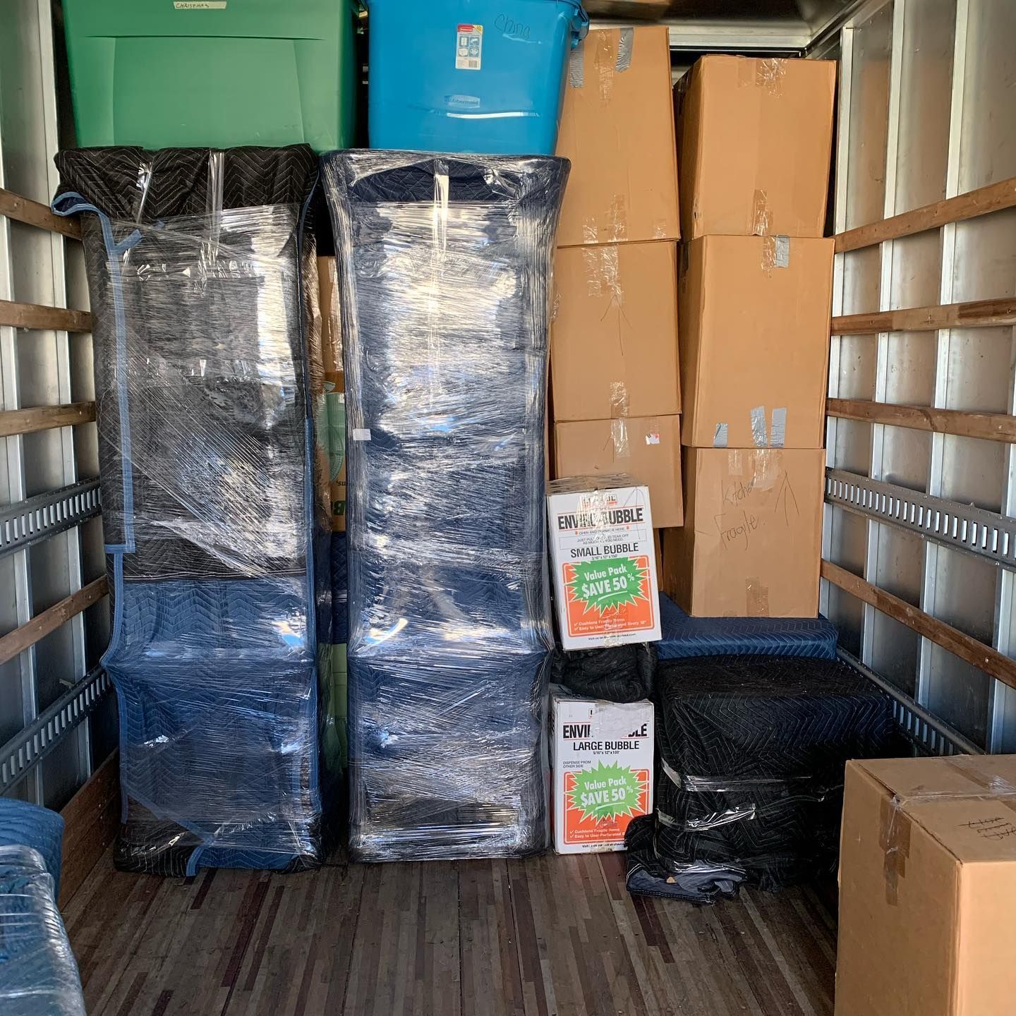 Packed moving truck with boxes, wrapped furniture, and storage bins inside.