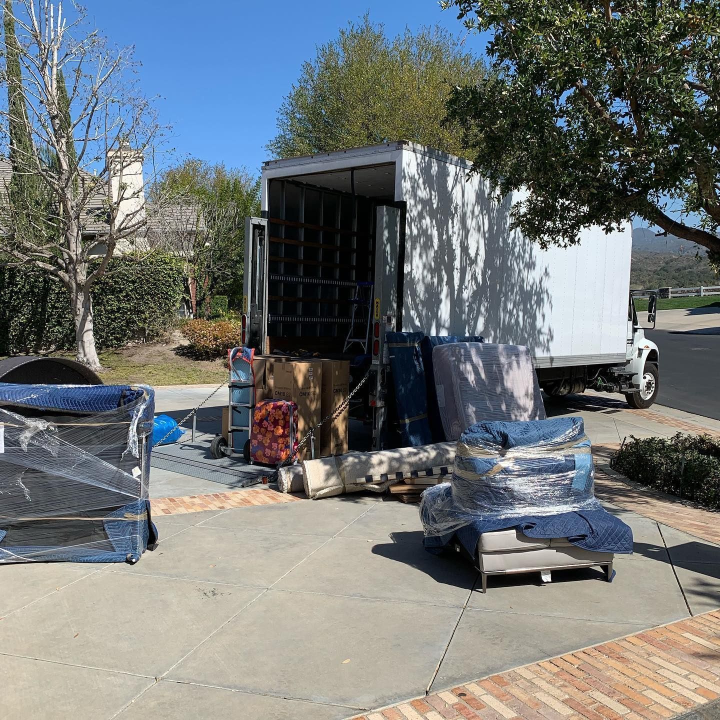 Movers unloading wrapped furniture from a white moving truck on a driveway