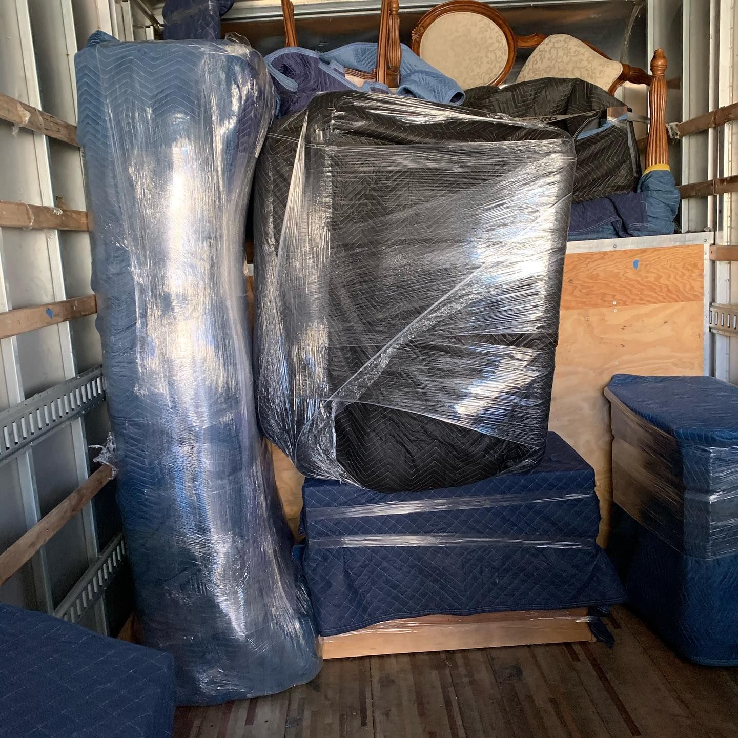 Wrapped furniture and stacked boxes loaded inside a moving truck, covered in blue and black plastic.