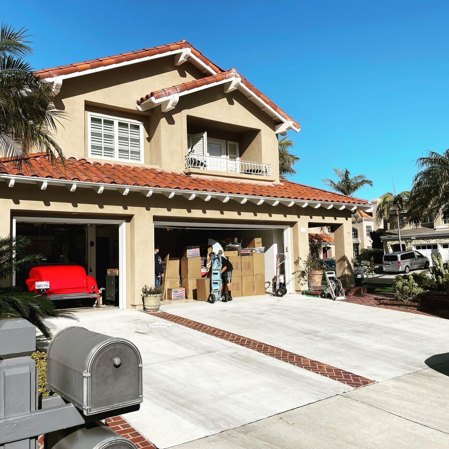 Two-story house with red roof, open garage, and a person standing in the driveway under a clear blue sky
