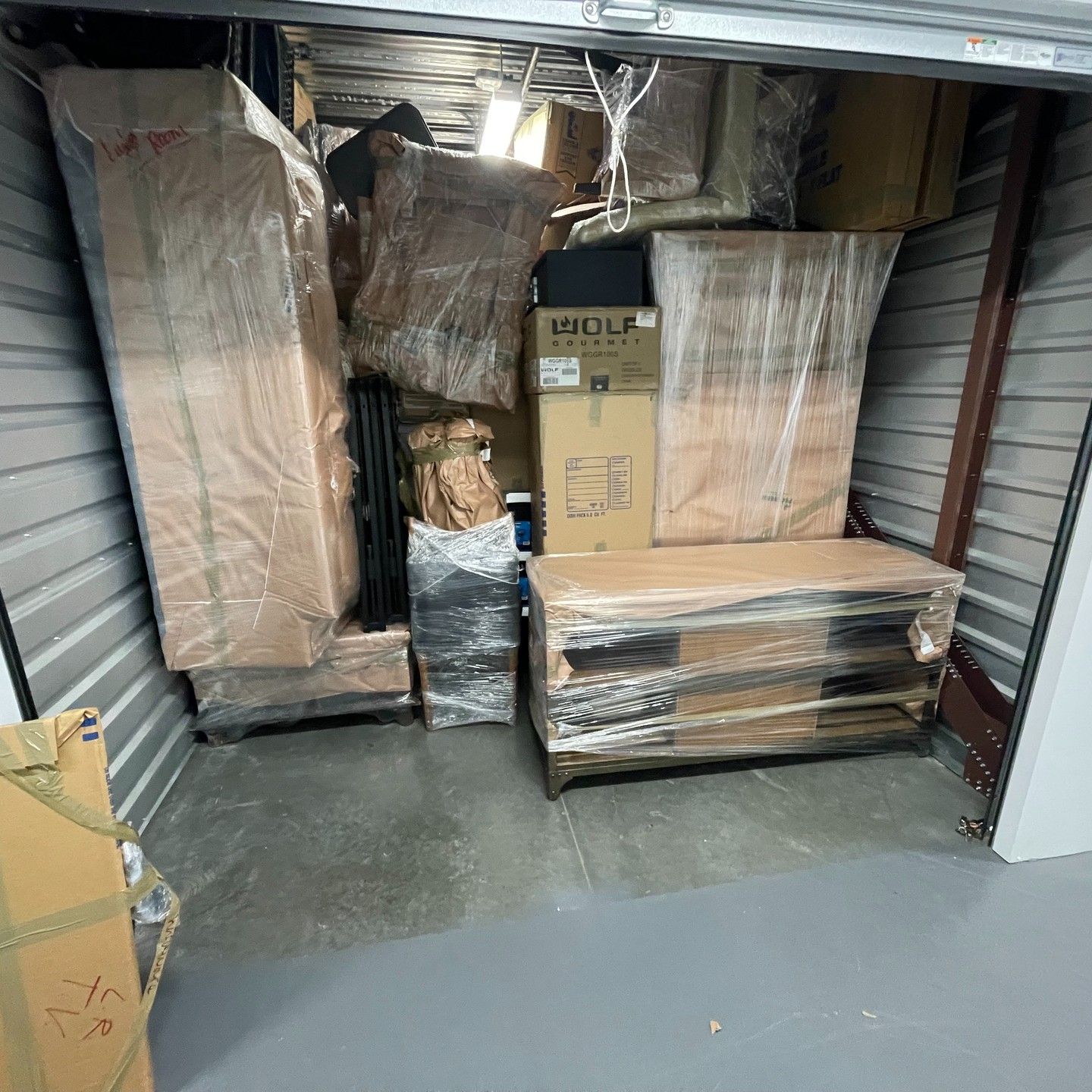 Storage unit filled with wrapped furniture and boxes, tightly packed on metal shelving