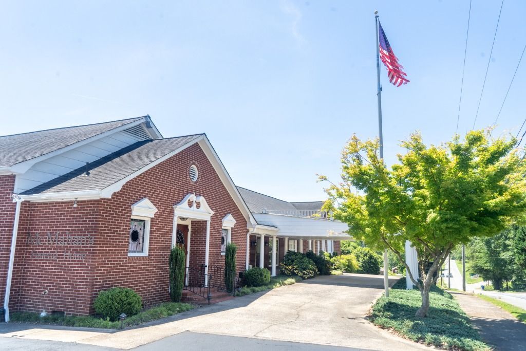 Red brick building with an American flag flying, driveway, and tree.