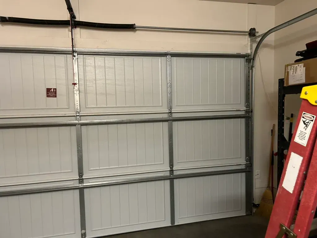 Interior of a garage with a closed white sectional door and a red ladder leaning on the right side