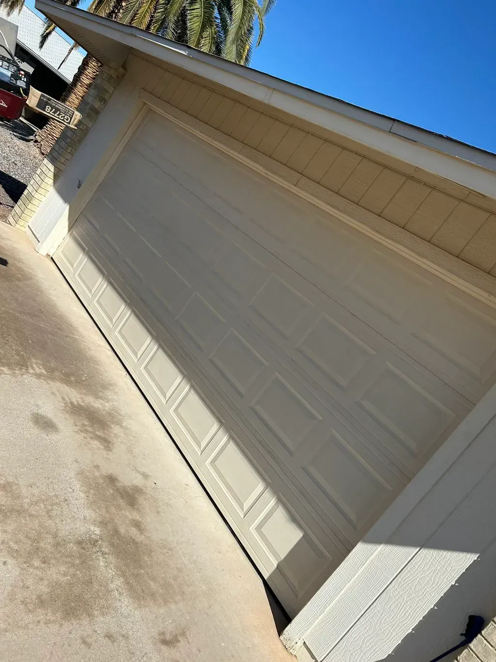 Tan garage door on a beige house, viewed at an angle in bright sunlight.