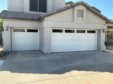 Suburban house with two white garage doors and a wide concrete driveway