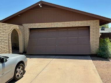 Single-story house with tan brick facade, brown garage door, and a driveway under a clear sky