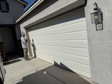 Person standing by a white garage door in a sunlit driveway