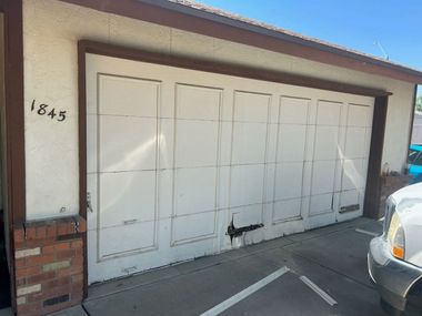 White garage doors on a stucco building with house number 1845 and a parked car at right