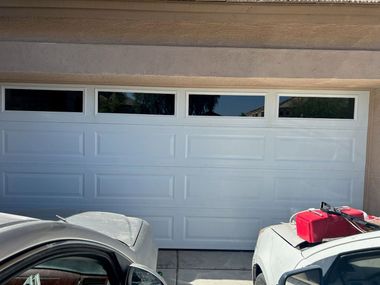 White garage door with four small windows, seen between two parked cars in a driveway.