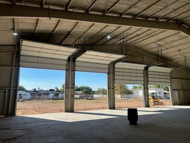 Empty industrial warehouse with large open garage doors and sunlight streaming onto the concrete floor.