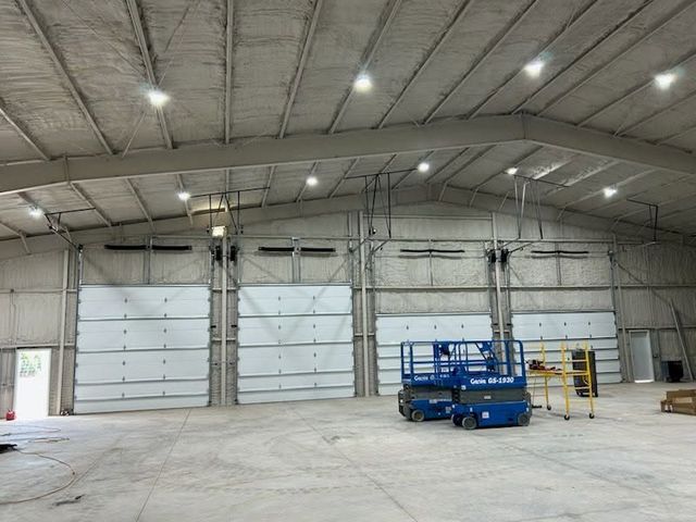 Empty warehouse interior with large white roll-up doors and a blue scissor lift on the concrete floor