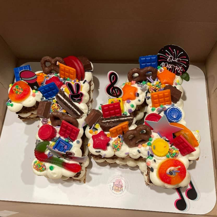 A number 14 cake decorated with colorful assorted candies, chocolates, pretzels, and musical note toppers in a box.