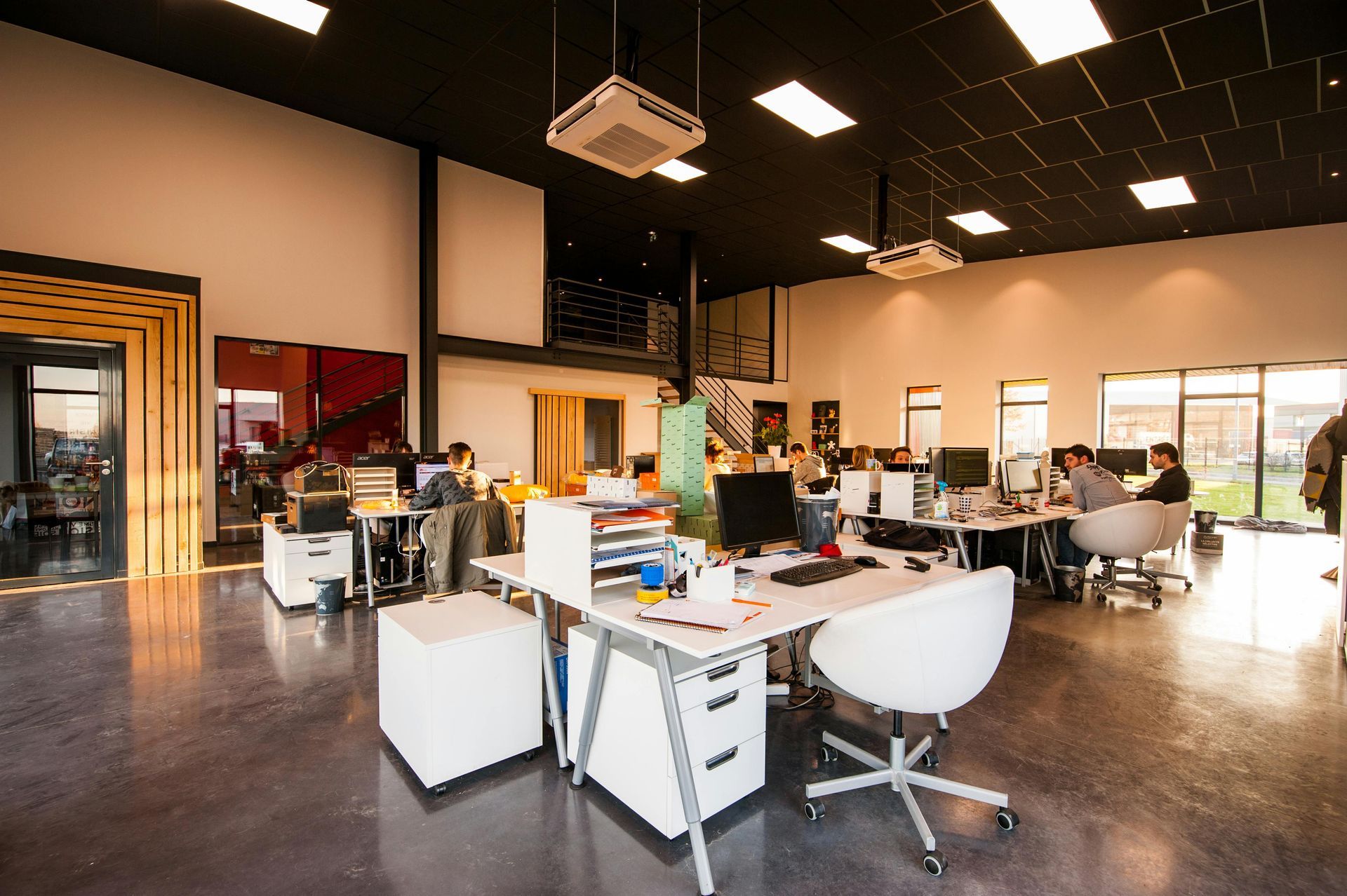 Modern open-plan office with desks, computers, and several people working under bright lights