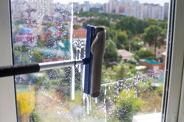 Window cleaner’s squeegee on a wet glass window with blurred city buildings outside