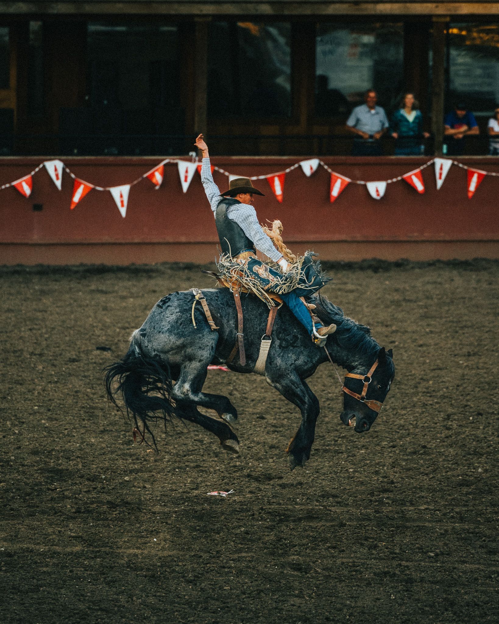 A man is riding a bucking horse in a rodeo arena.