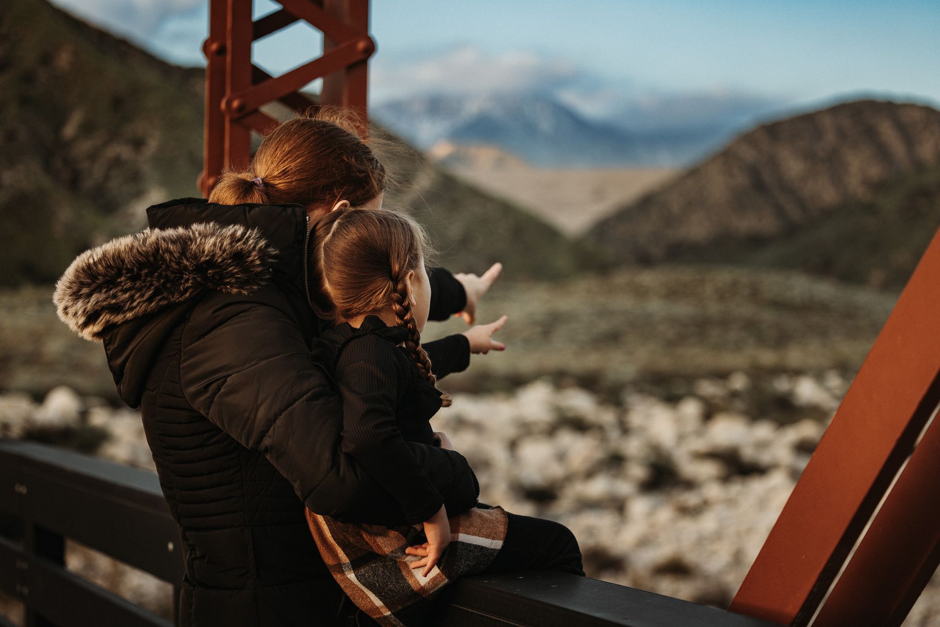 A woman is holding a child in her arms and pointing at the mountains.