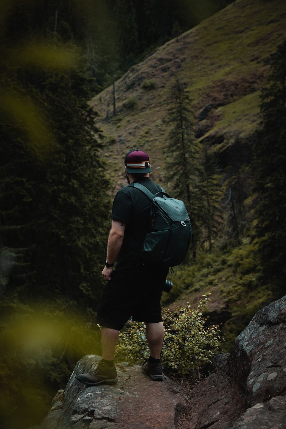 A man with a backpack is standing on a rock in the woods.