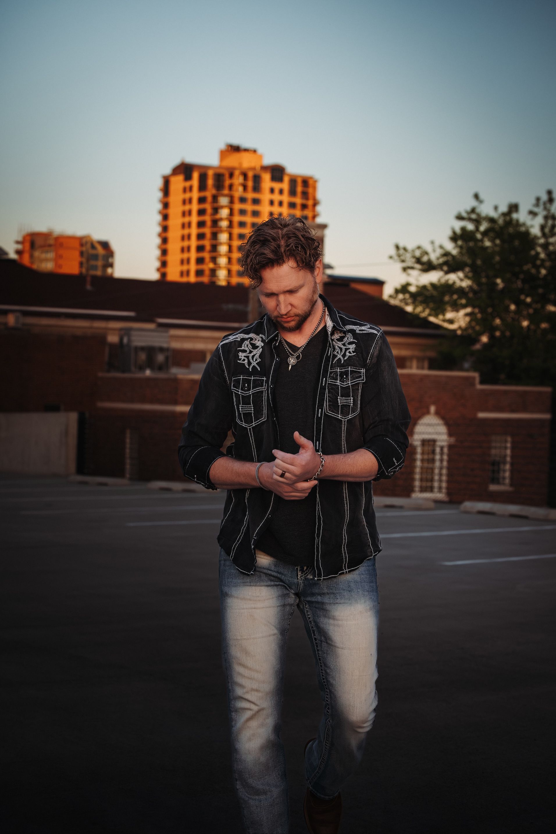 A man in a black shirt and jeans is standing in front of a building.