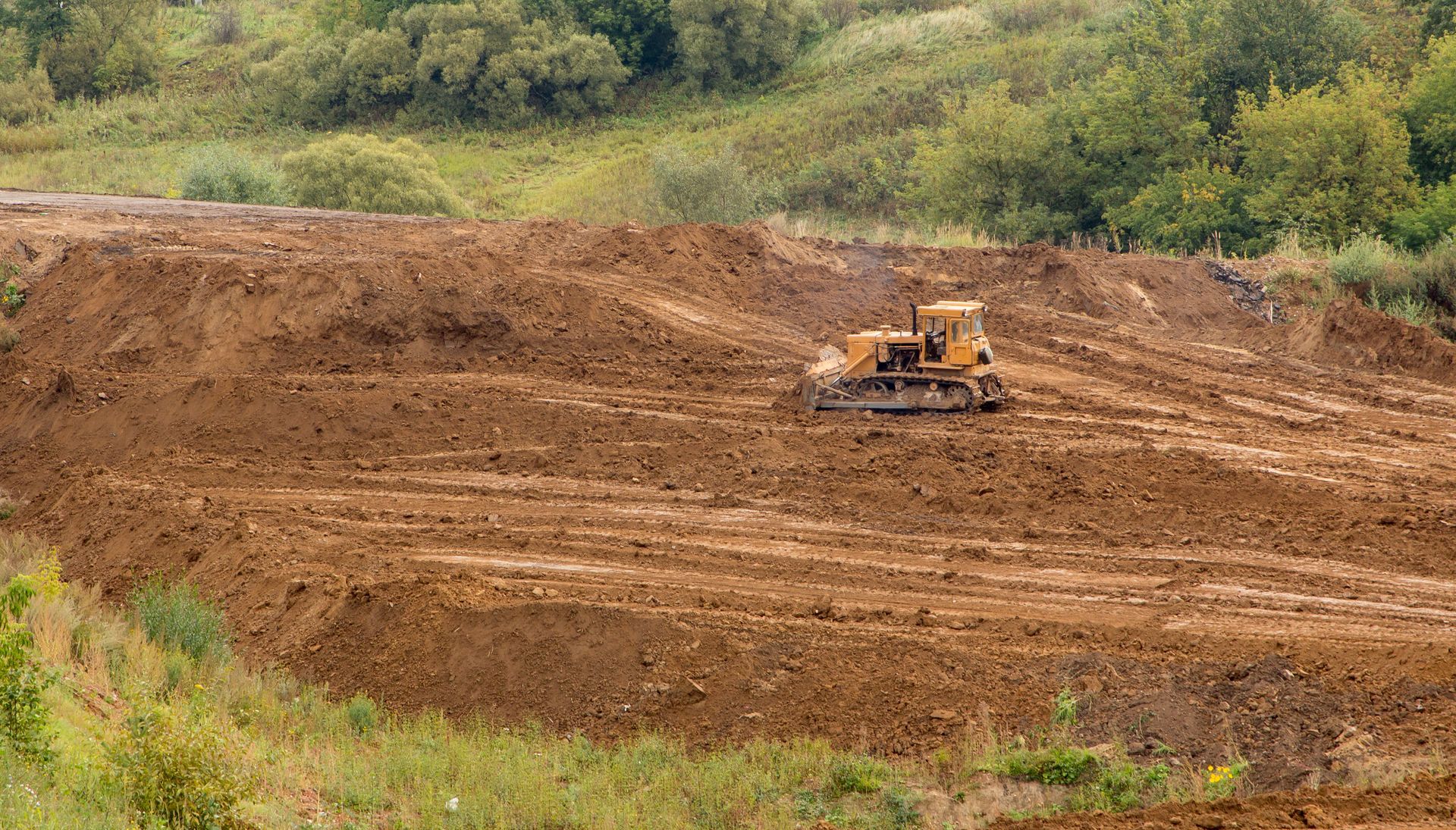 Bulldozer leveling a large brown dirt field with green trees in the background Bulldozer leveling a large brown dirt field with green trees in the background