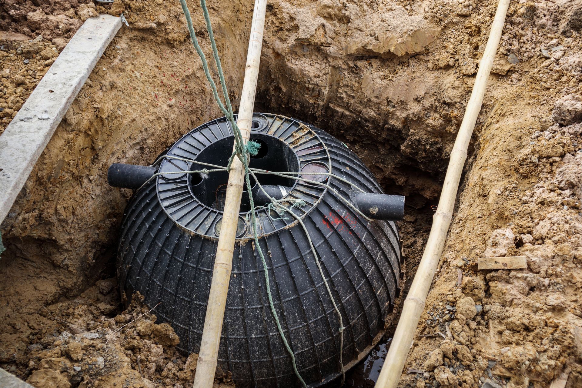 Black septic tank being installed in a dug trench with pipes and wooden braces Black septic tank being installed in a dug trench with pipes and wooden braces