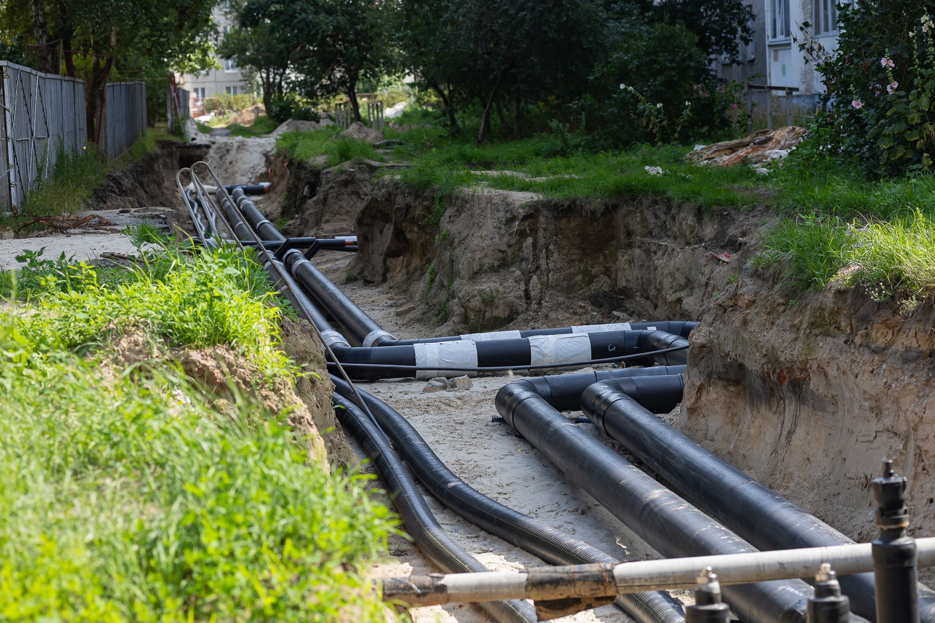 Underground utility pipes in a trench beside a grassy path and trees Underground utility pipes in a trench beside a grassy path and trees