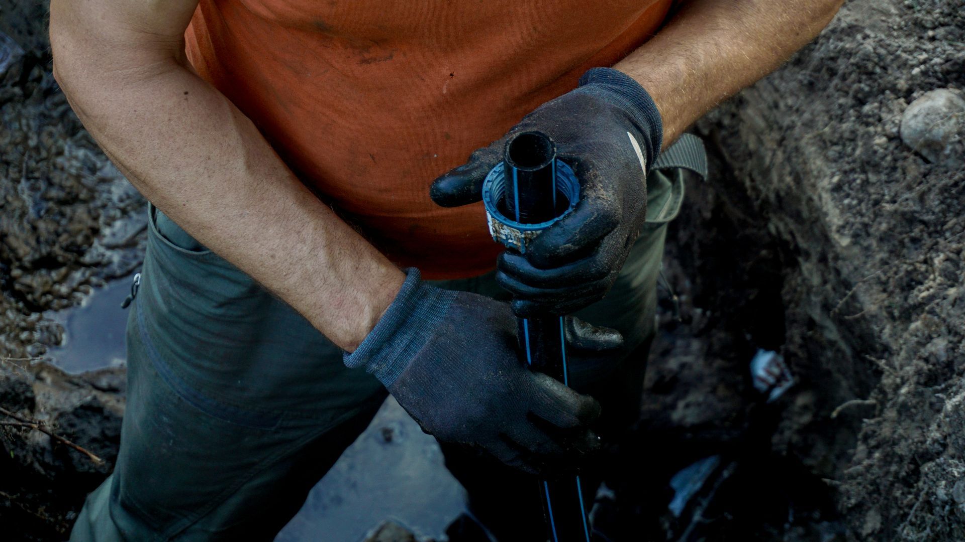 Gloved person holding a blue pipe inside a rocky trench Gloved person holding a blue pipe inside a rocky trench